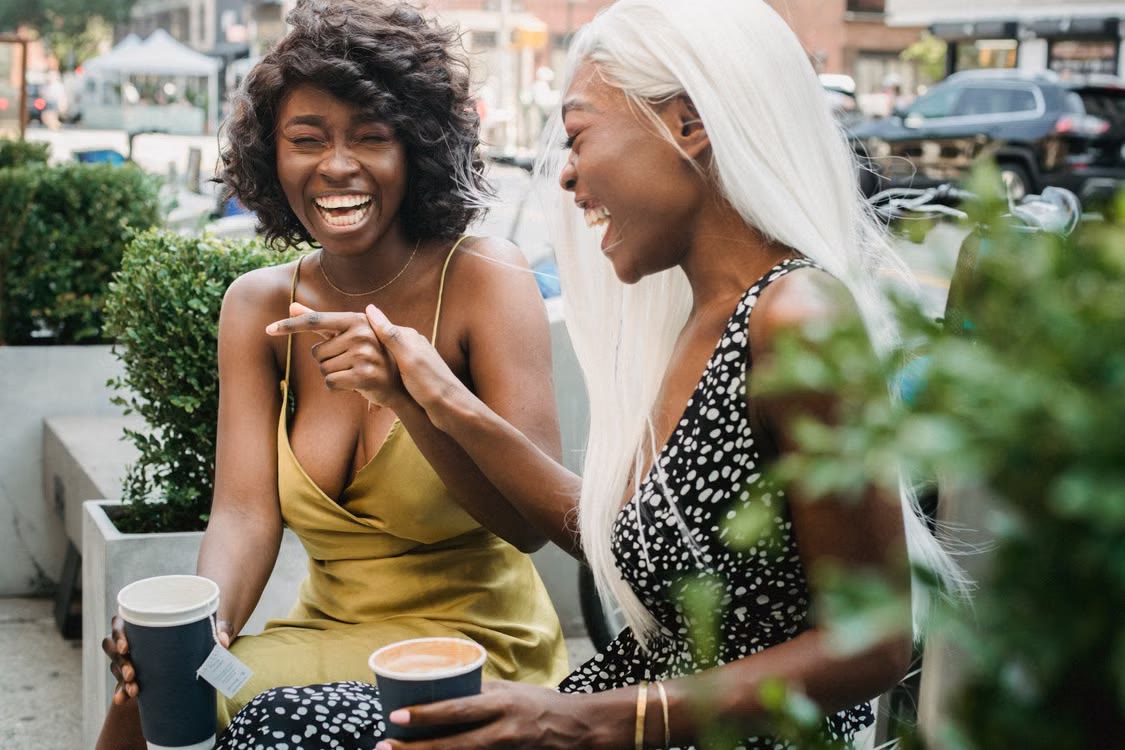 Two friends laughing together over coffee outdoors.