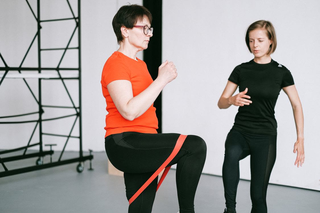Woman practicing a resistance-band exercise with guidance from a trainer.